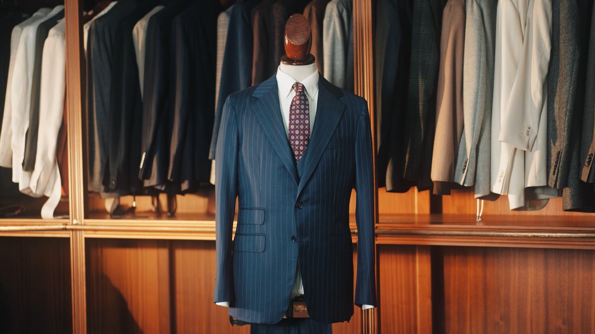 Costume à fines rayures bleu nuit, sur mannequin, devant les portants de la boutique