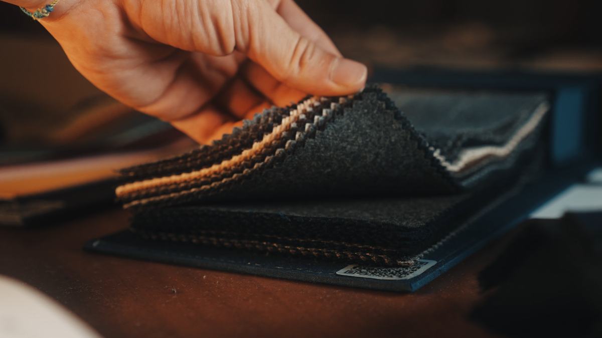 Une main soulève les échantillons d’un carnet de tissus posé sur une table de cuir