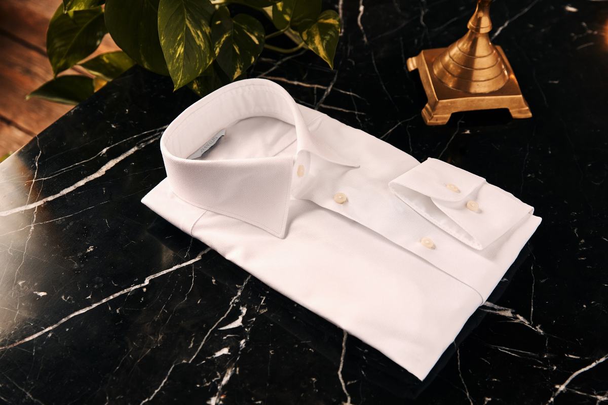 Une chemise blanche pliée, col et poignet posés dessus, sur un plateau de marbre noir veiné
