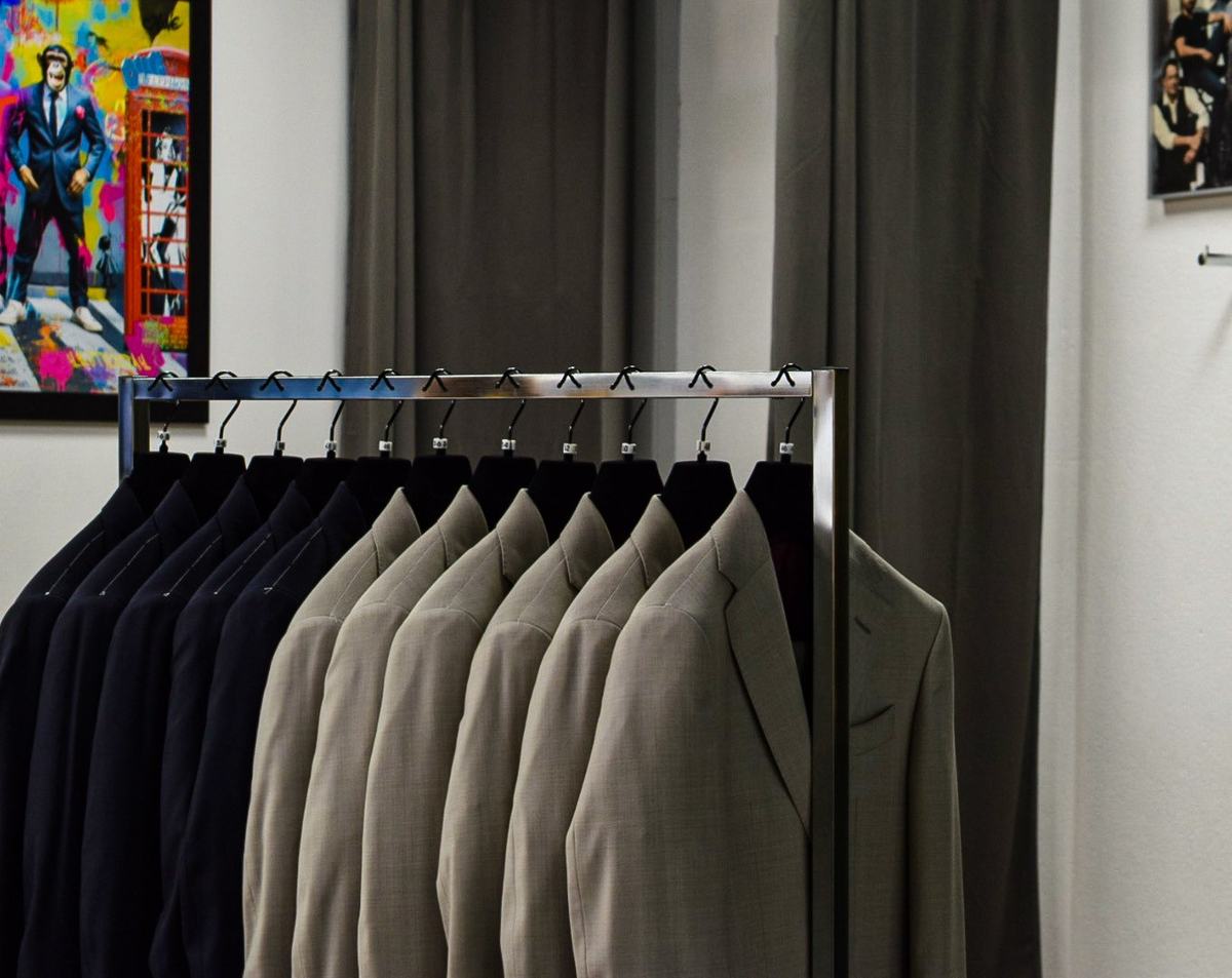 Deux séries de vestes, bleu nuit puis beige, devant un lourd rideau gris taupe, toile colorée d’un singe en costume à gauche