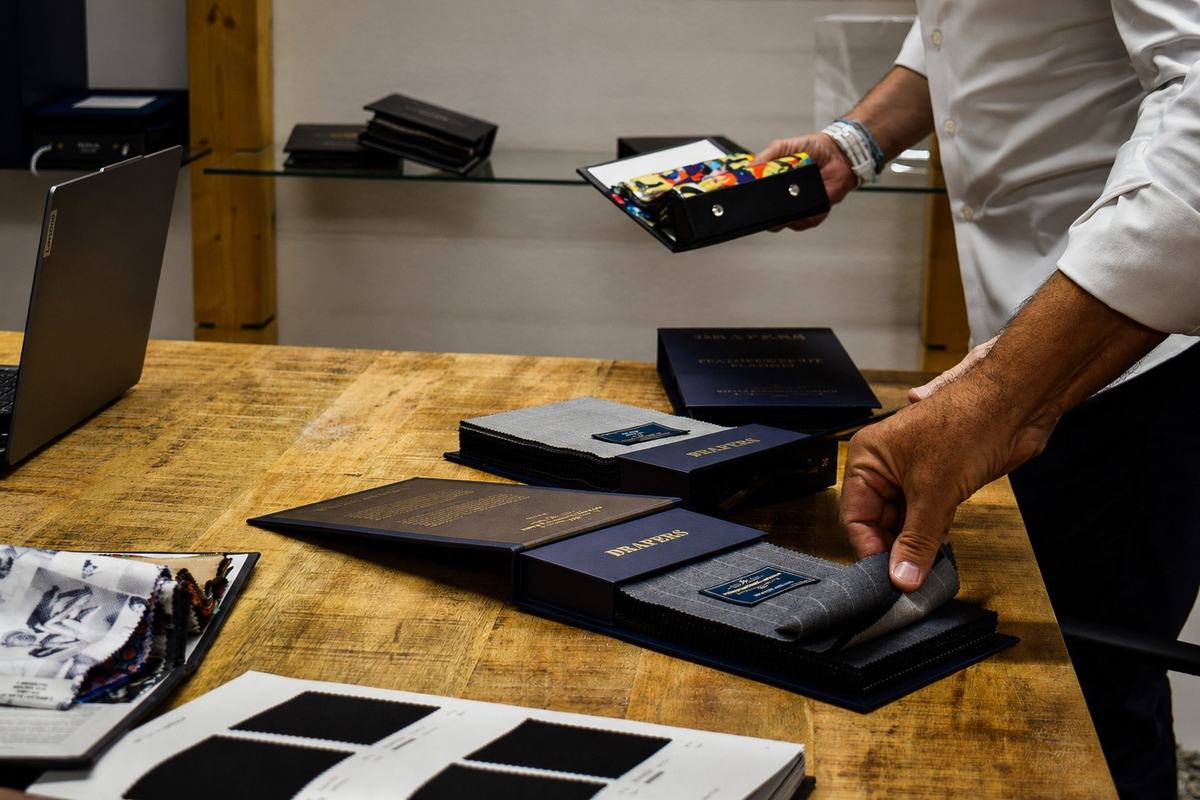 Un homme feuillette des classeurs d’étoffes sur une table de bois, un carnet de soies colorées ouvert dans la main