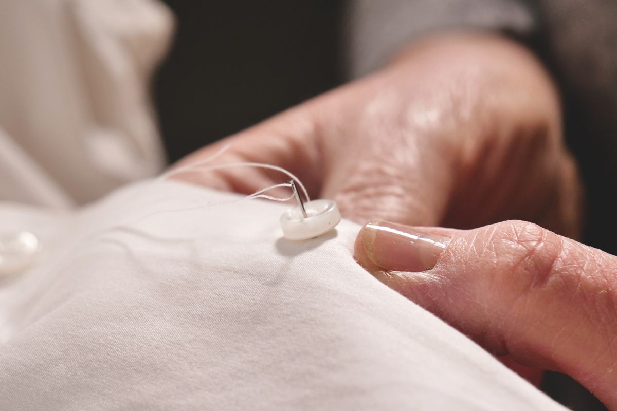 Un bouton de nacre cousu à la main sur une étoffe blanche, l’aiguille encore en place