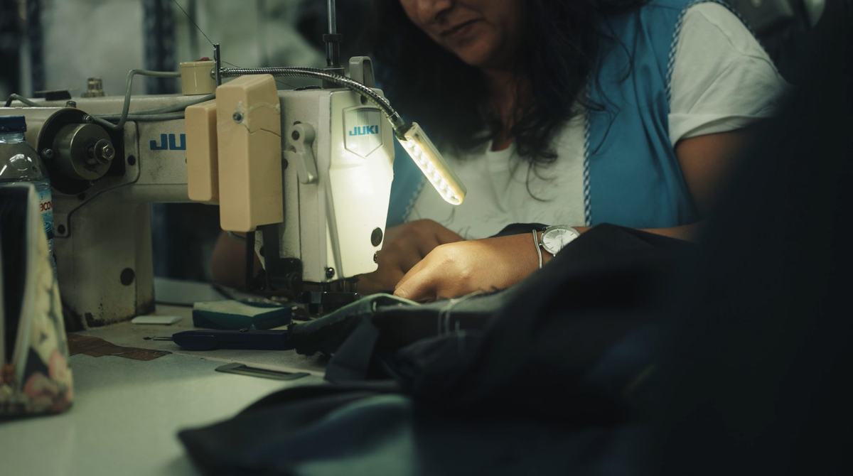Une couturière guide une étoffe sombre sous l’aiguille éclairée de sa machine