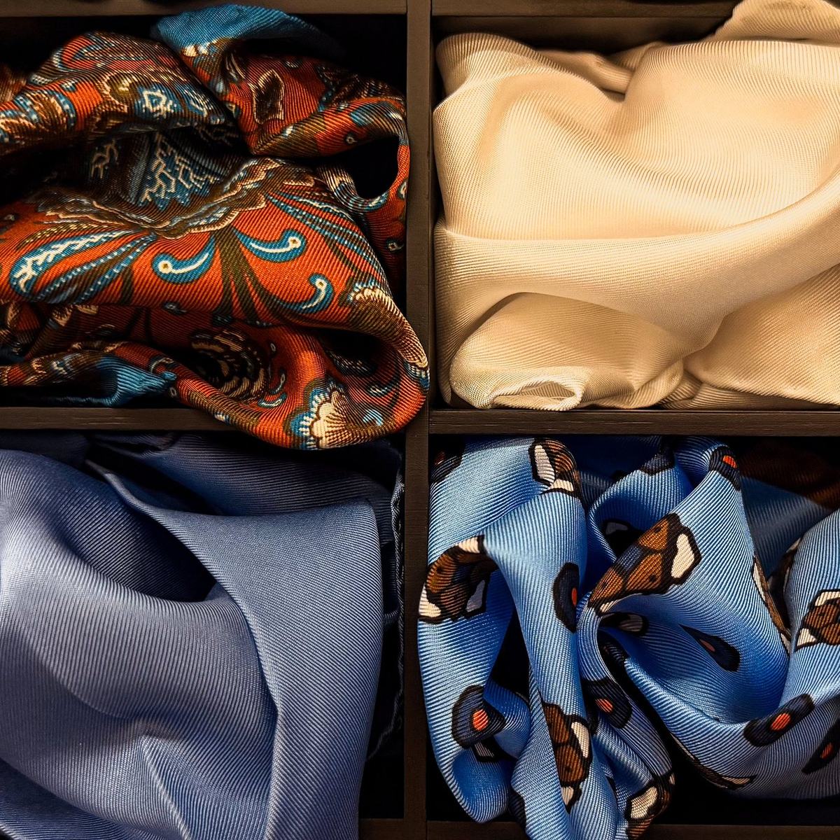 Quatre pochettes glissées chacune dans son casier carré, une orangée imprimée, une crème, deux bleues