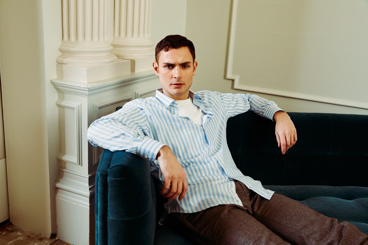 Chemise à rayures bleues et blanches portée ouverte sur un tee-shirt, homme allongé sur un canapé de velours