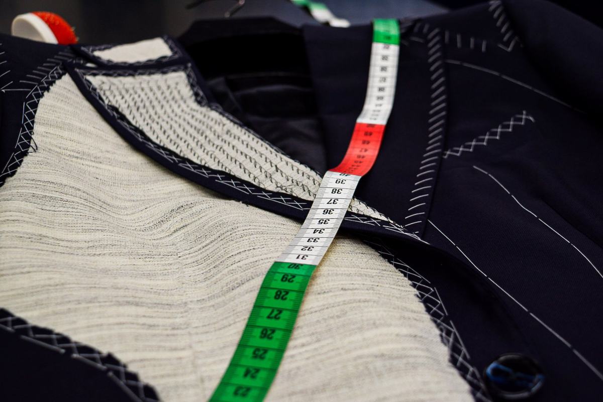 Gros plan sur le plastron de toile écrue d’une veste marine, ses rangées de piqûres et ses points de bâti blancs sous un mètre ruban